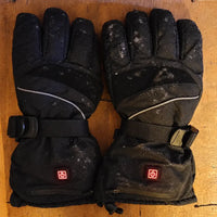 Pair of The Warm Chapter heated gloves resting on a wooden table