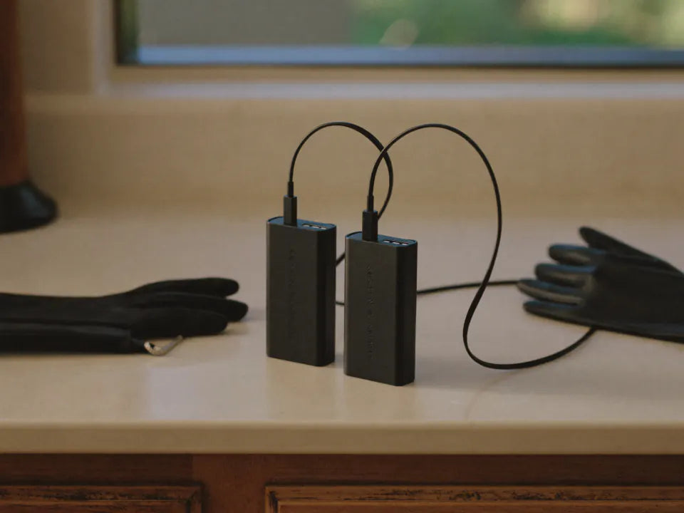 Two battery packs charging on a kitchen worktop beside folded gloves